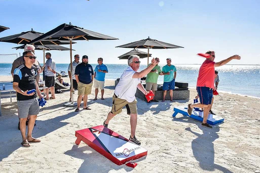 Attendees playing cornhole on the beach during a group program