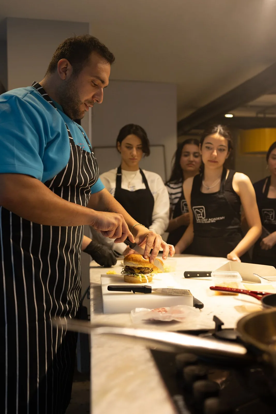 A chef demonstrating food preparation to participants in aprons
