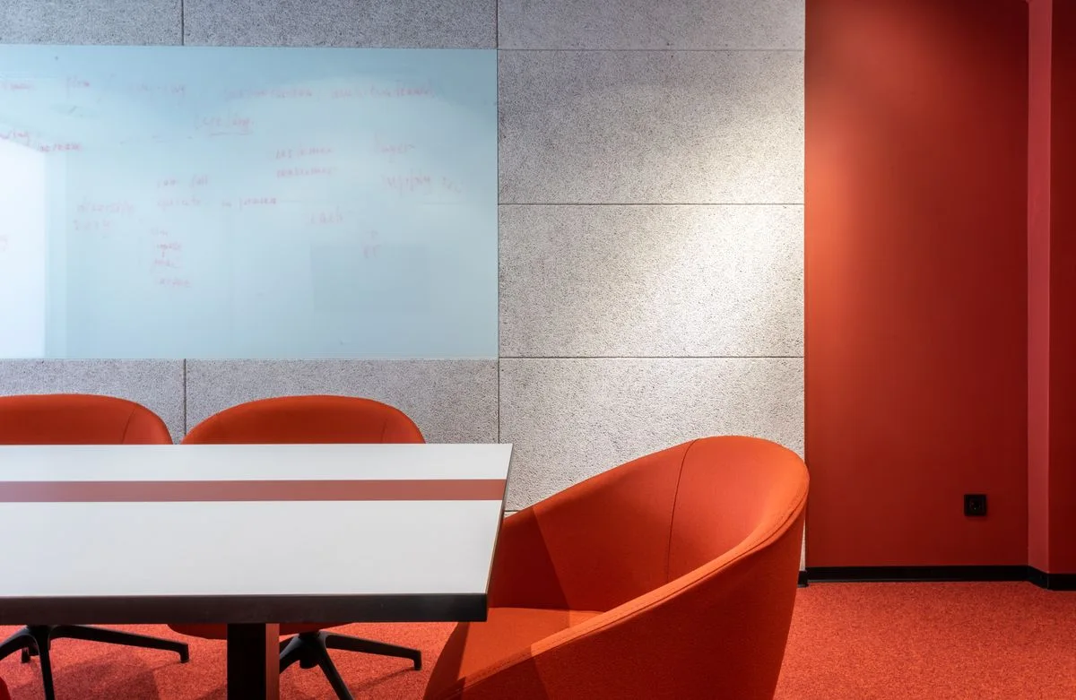 A meeting table with orange chairs and a whiteboard wall