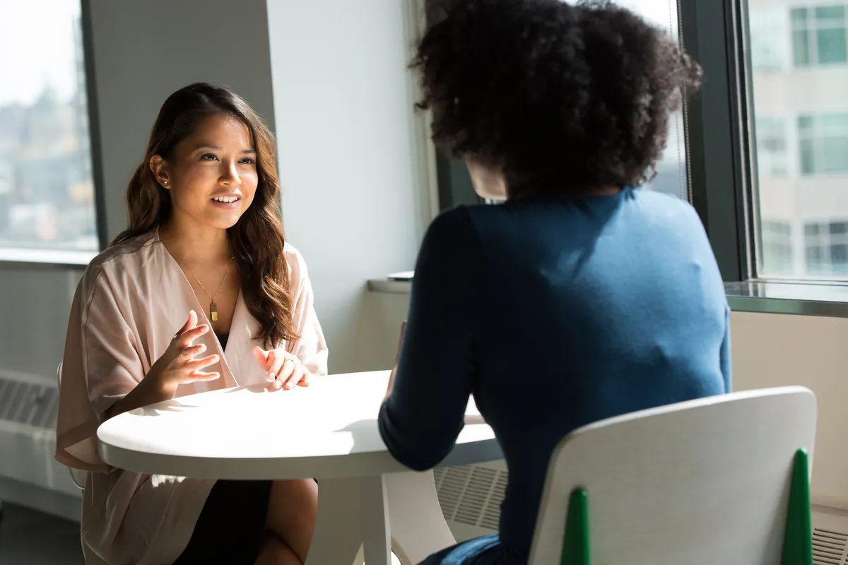 Two colleagues talking across a small table by a window.
