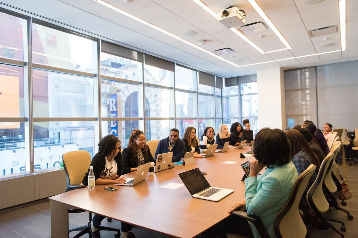 A team with laptops around a long table in a glass-walled meeting room.