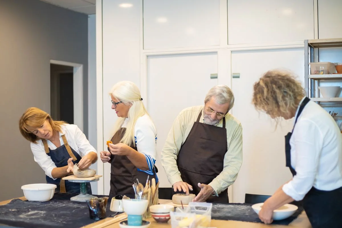 Adults learning pottery together around a workshop table