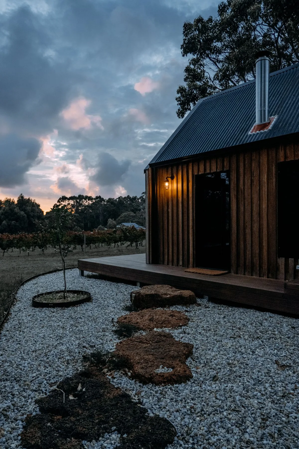 A wooden house with a deck beside trees and a garden